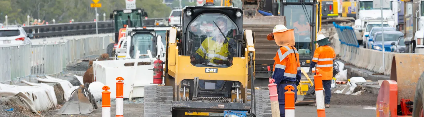 Construction workers operating various machines and equipment on a busy roadwork site, ensuring safety and progress.