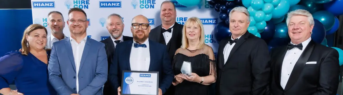 Employees smiling and holding awards, standing in front of a company logo backdrop at a recognition event.
