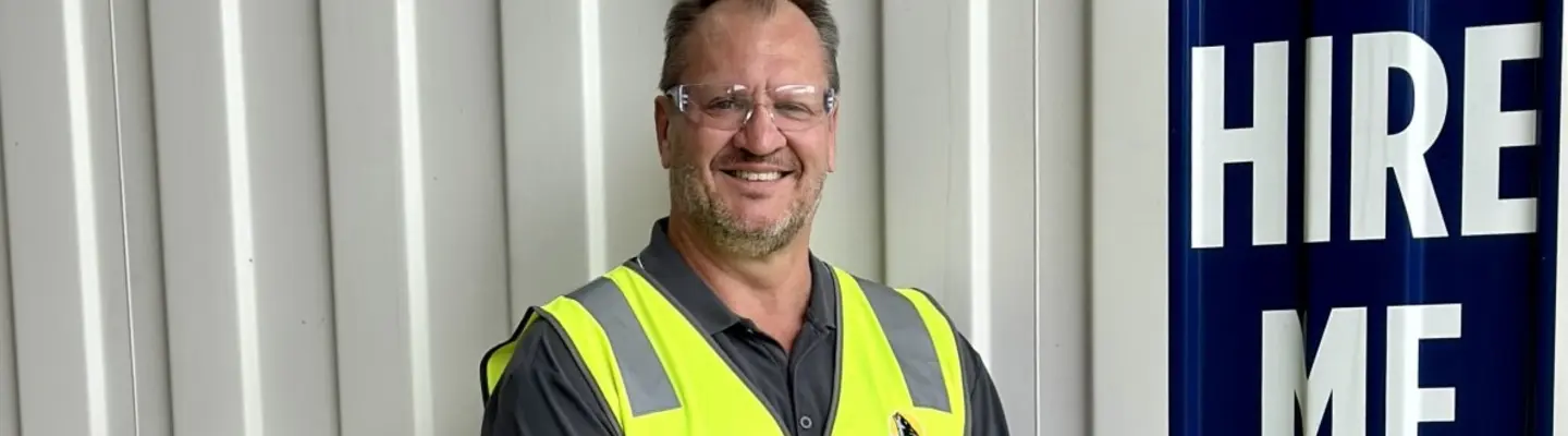 Man standing and smiling confidently in an outdoor setting, conveying positivity and professional presence.
