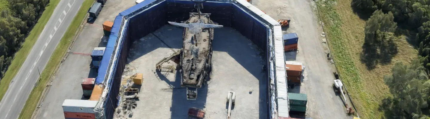 Ship surrounded by stacked shipping containers painted blue, creating a temporary blue screen setup for filming or visual effects work.