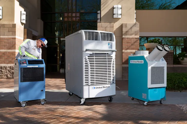man inspecting a portable heater next to two other portable air conditioner units