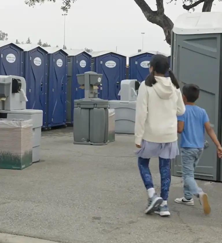 Two children walking to the porta potties at a county fair