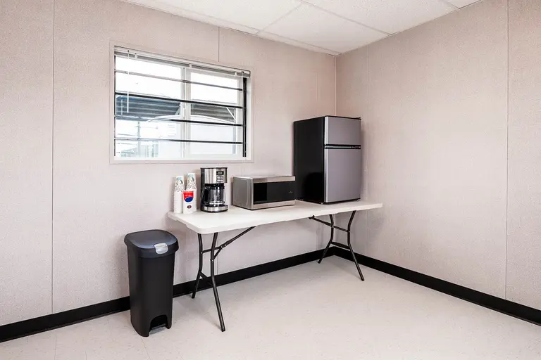 Refrigerator, microwave, coffeemaker and coffee cups on a table with a trashcan nearby
