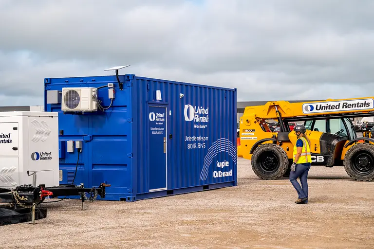 A United Rentals employee walking to a blue supplies on demand container at a jobsite