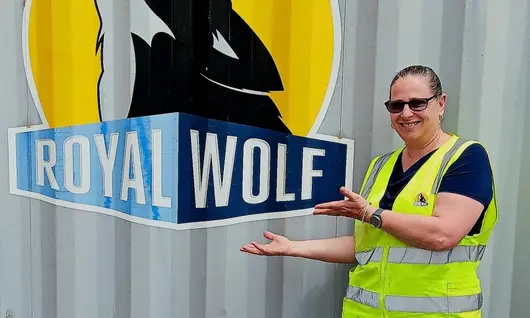 Woman standing and smiling in front of a company logo, representing professionalism and company pride.
