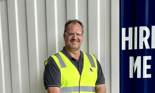 Man standing and smiling confidently in an outdoor setting, conveying positivity and professional presence.